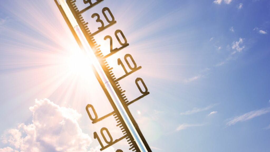 Termômetro vertical mostrando temperaturas sob luz solar com céu azul ao fundo.